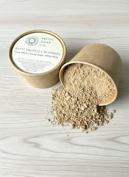 Bath truffle crumbles in an open container on a wooden surface with 'Pretty Soap Co.' packaging.