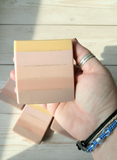 Hand holding a beige and pink soap bar on a wooden surface