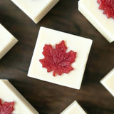 several soap bars scattered on a dark wood table.  Soap is white with a red maple leaf in the center.