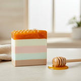 Colorful striped soap  with a honeycomb design on top, sitting on a light wood surface with window and houseplants in the background