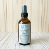 Bottle of Juniperberry and Pine room spray from Pretty Soap Co. on a wooden surface