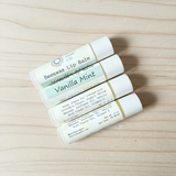 Four lip balm tubes labeled 'Vanilla Mint' on a wooden surface