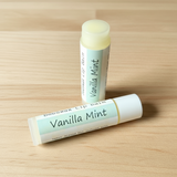 Two Vanilla Mint lip balms on a wooden surface