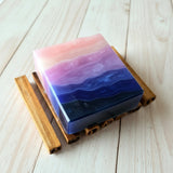 A handcrafted soap with layers of purple, blue, and pink, placed on a wooden surface.