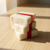 Two square soap bars with a dark pink stripe on a wooden surface