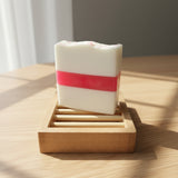 Bar of soap with a pink stripe on a wooden soap dish against a wooden background