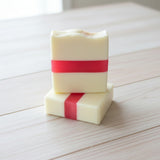 Two stacked soap bars with a dark pink  stripe on a wooden surface