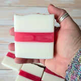 Hand holding a white with a pink striped bar of soap with a wooden background