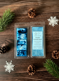 Packaged blue wax melts labeled 'Winter Wonderland' on a wooden surface with pine cones and snowflakes.