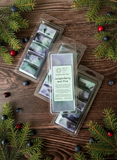 Packaged wax melts with 'Juniperberry and Pine' scent on a wooden surface with pine branches and berries.
