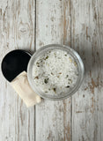 Container of bath salts with herbs on a wooden surface.
